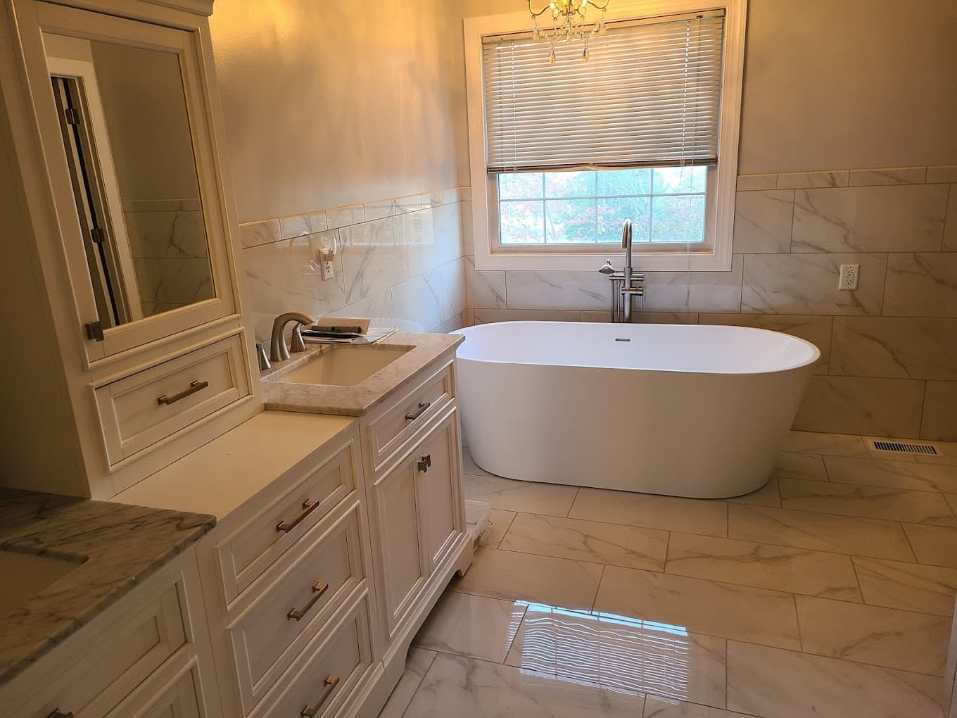 Remodeled master bathroom with a freestanding soaking tub, marble-look tile and a white vanity